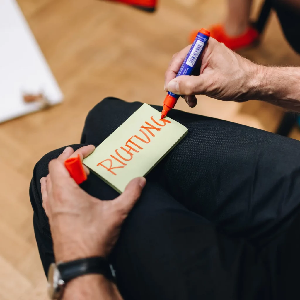 MINT Herangehensweise conceptk; Mann schreibt mit rotem Edding "Richtung" auf ein Postit.